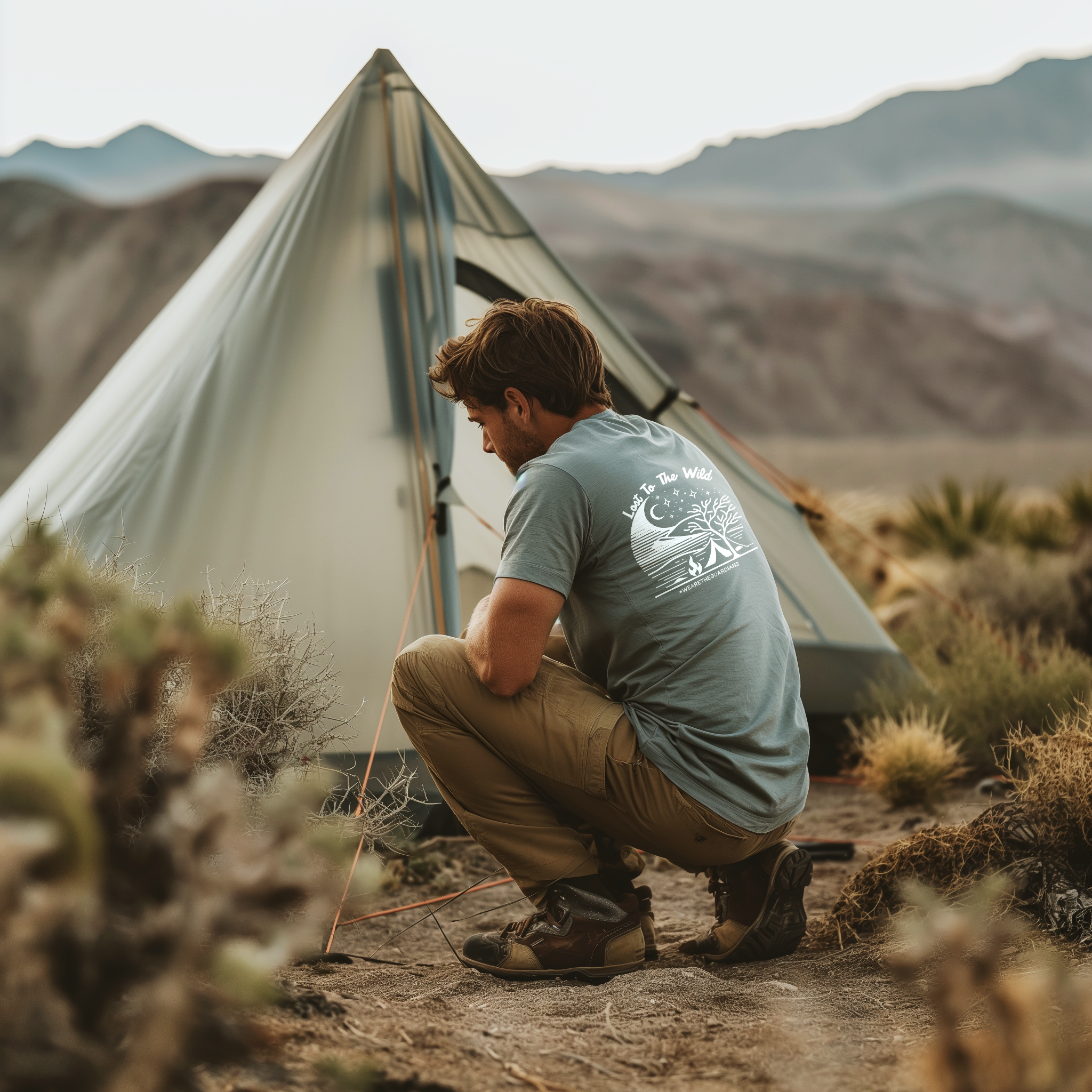 Man setting up camp in desert wilderness wearing the Bushcrafter - Lost To The Wild Men's Crewneck Tee 100% Cotton Steel Blue